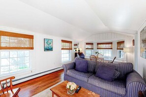 A living room with a striped sofa, a wooden coffee table with a vase, and a dining area with a table and chairs. - Charming island cottage near town & beaches (Edgartown)