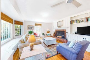 A living room with a fireplace, sofa, coffee table, and television. - Charming island cottage near town & beaches (Edgartown)
