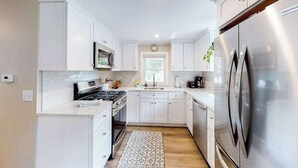 Une cuisine moderne avec des meubles blancs, des appareils en acier inoxydable et un tapis à motifs.