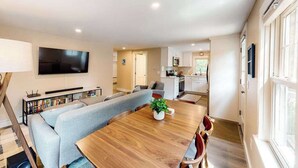 Un salon moderne avec une table à manger en bois, un canapé gris et un téléviseur à écran plat fixé au mur.