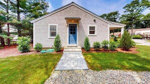 Une maison de plain-pied avec une porte bleue, un petit porche et une allée gravillonnée.