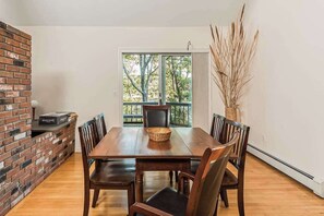 A dining area with a brick wall, a wooden table, and chairs. - Waterfront home with lovely lake views, great deck, sun porch & fireplace (Chatham)