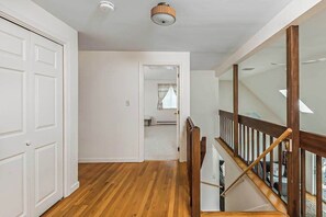 A hallway with wooden flooring, white walls, and a staircase with wooden railings. - Waterfront home with lovely lake views, great deck, sun porch & fireplace (Chatham)