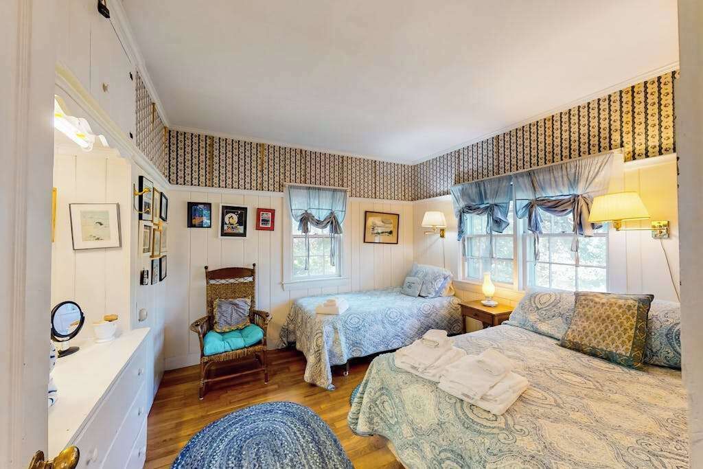 Ein Schlafzimmer mit zwei Betten, einem Sessel, einem Schminktisch und einem Spiegel.
