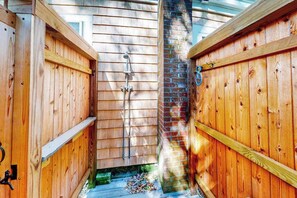 A wooden outdoor shower area with a brick wall and a metal showerhead. - Dog-friendly beach cottage on Harwich's main street with large lawn (Harwich Port)
