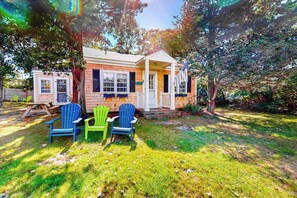 Ett litet hus byggt av tegel med en veranda, två Adirondack-stolar och en flagga.