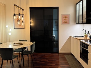 Eine moderne Küche mit einem schwarzen Kühlschrank, einem Marmortisch und einer Pendelleuchte.
