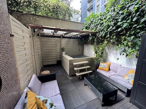 Eine Terrasse mit einer Couch, einer Bank, einem Tisch und einer Pergola mit Lichterketten.