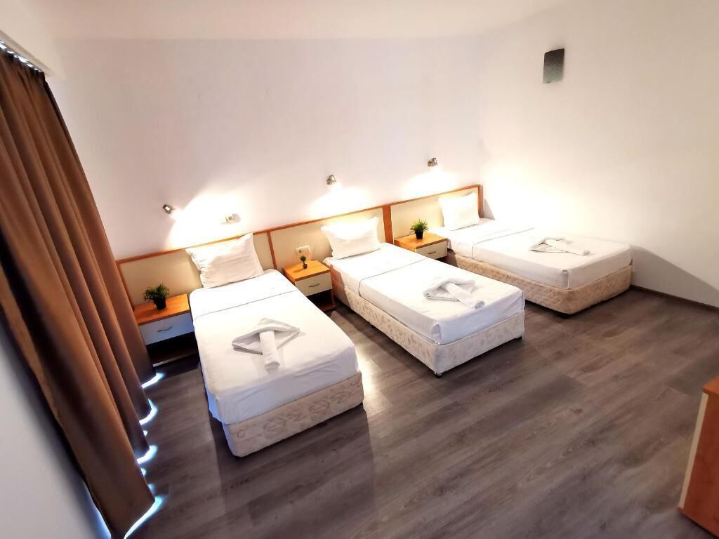 Habitación de hotel con tres camas, suelo de madera y lámparas de noche.