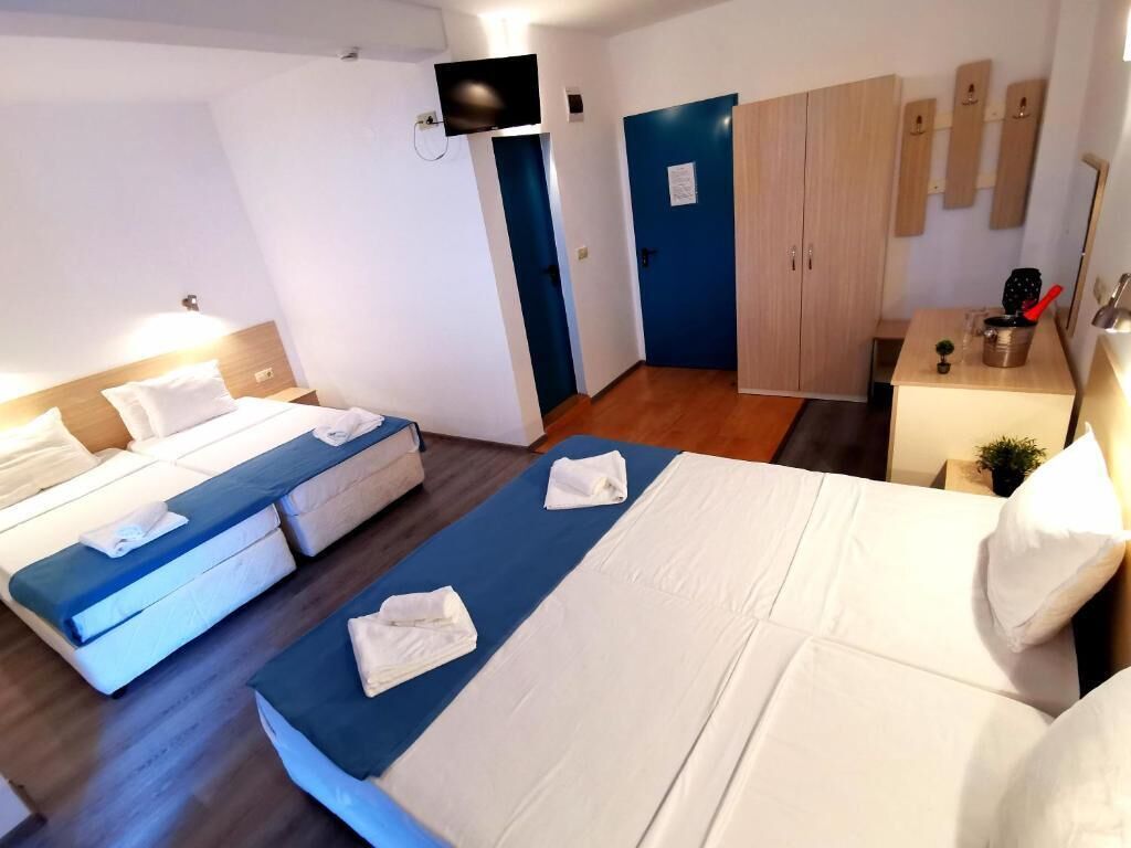 Ein Hotelzimmer mit zwei Betten, einem Fernseher, einem Kleiderschrank und einem kleinen Tisch mit einer Pflanze.