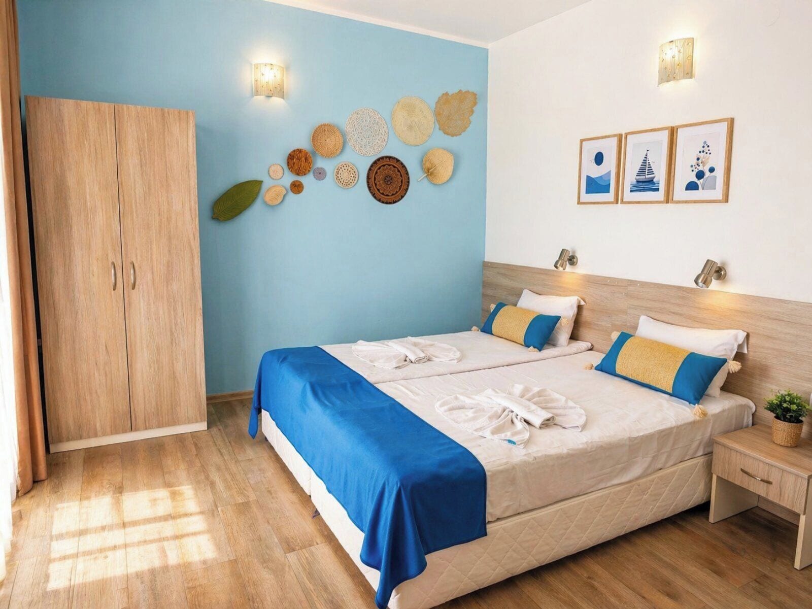 Una cama doble con colcha azul y blanca, un armario de madera, y decoración en la pared que incluye un colgador circular y cuadros enmarcados.