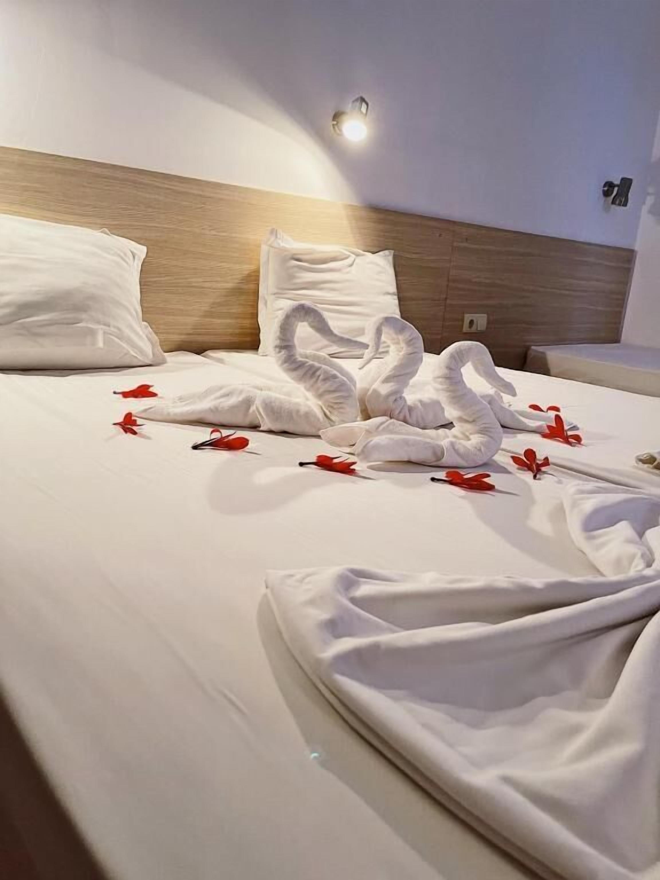 A neatly made bed with white linens, a wooden headboard, and a wall-mounted light fixture.