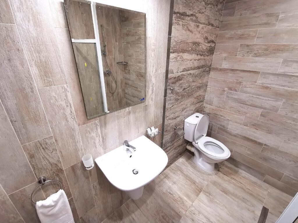 A bathroom with a sink, mirror, toilet, and marble tiles.