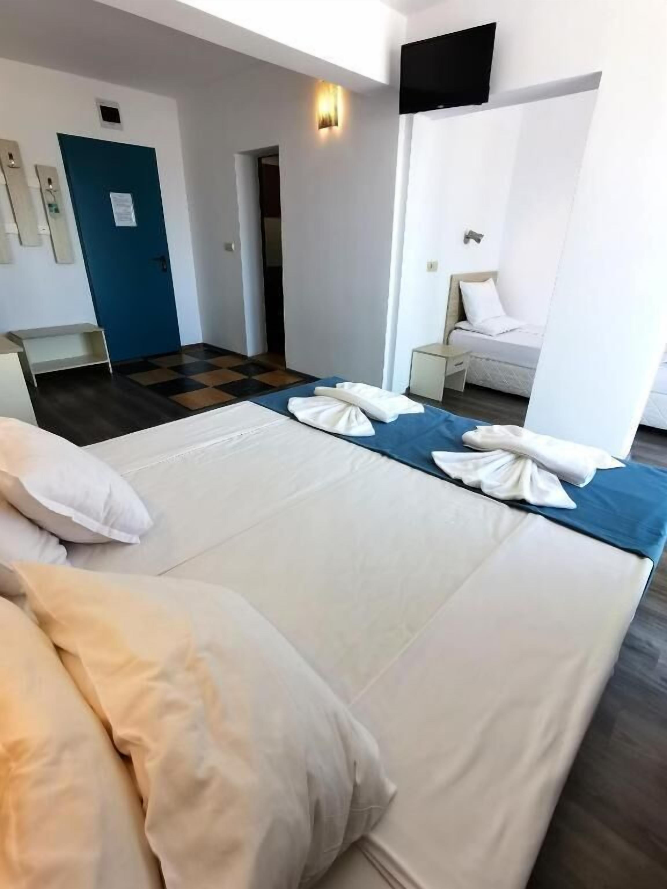 Habitación de hotel con dos camas, un escritorio, una silla, una puerta azul y un televisor de pantalla plana montado en la pared.