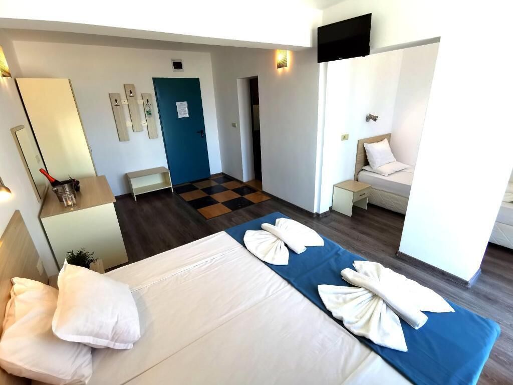 A hotel room with a bed, a desk, a chair, a TV, and a door.