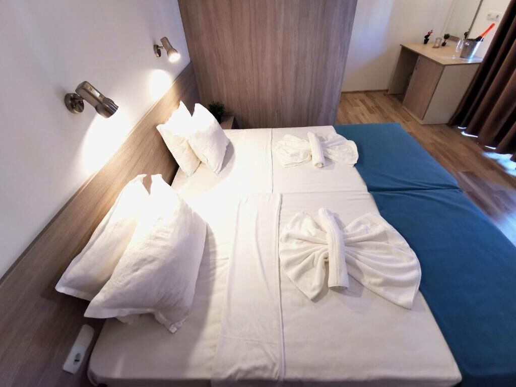 A neatly made bed with white linens and towels, a bedside table with a lamp, and a wooden headboard.