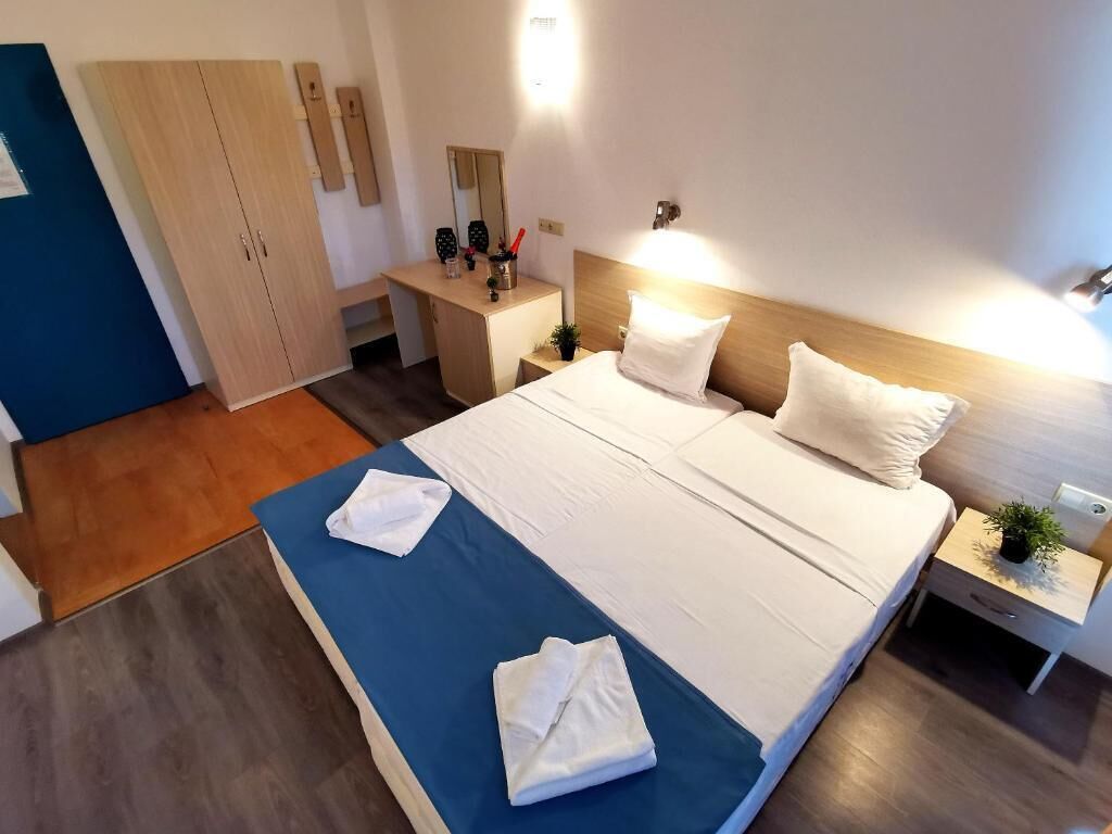 A hotel room with a bed, bedside tables, a wardrobe, and a desk with a chair.