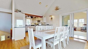 Une cuisine moderne avec des meubles blancs, un coin repas avec une table et des chaises blanches, et une grande porte-fenêtre coulissante donnant sur un espace extérieur.
