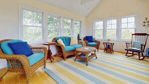 Une pièce meublée de meubles en osier, avec un tapis à rayures et de grandes fenêtres.