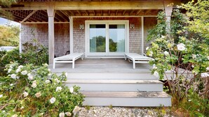 Une véranda couverte avec deux fauteuils de jardin blancs, une pergola en bois et un mur en briques.