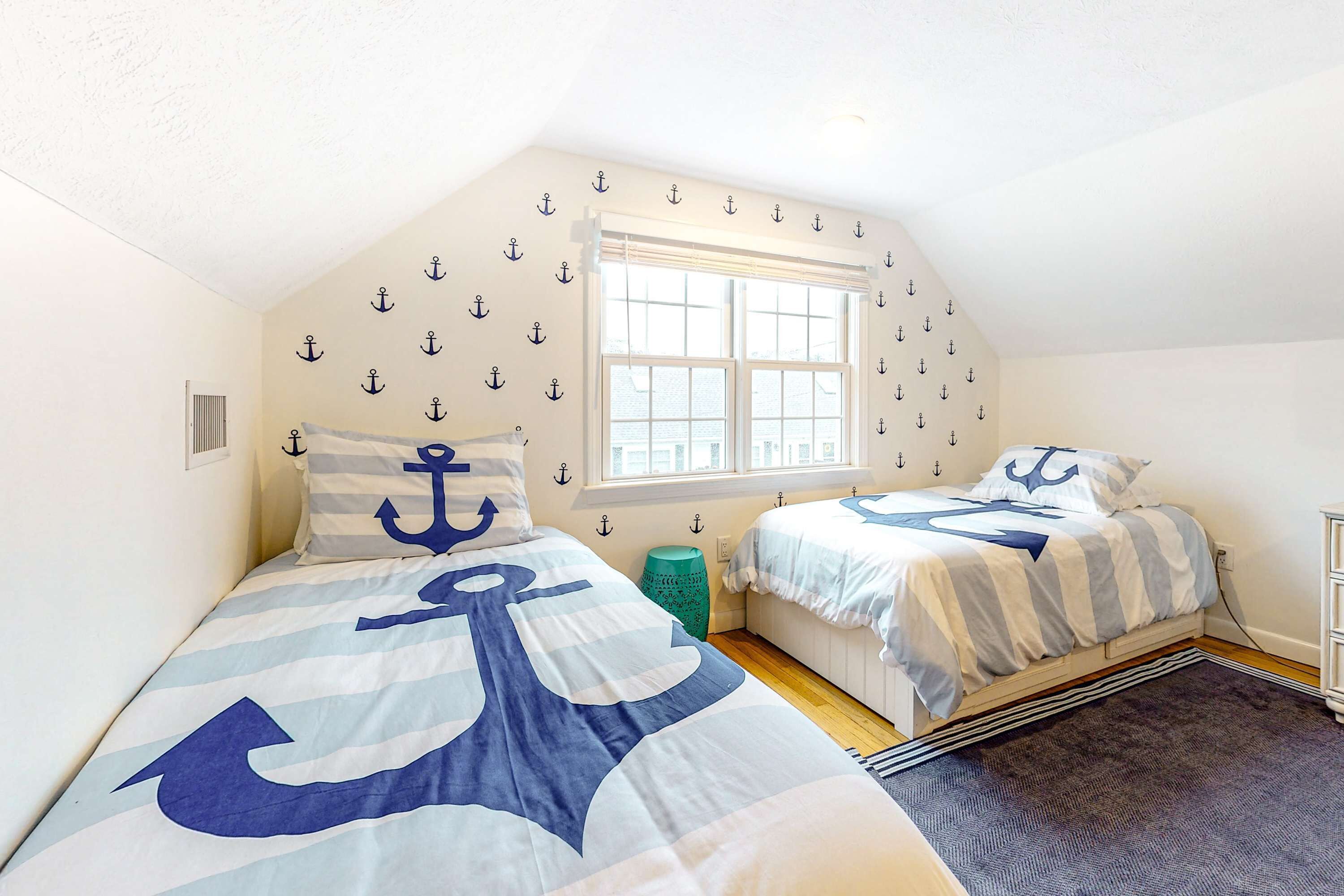 Een slaapkamer met twee bedden, een raam en decoratie met anker thema.