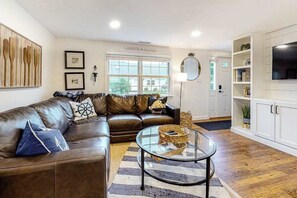 Ein Wohnzimmer mit einer Ledersofa, einem Glastisch, einem Streifen Teppich, einem Fernseher und einem Bücherregal.