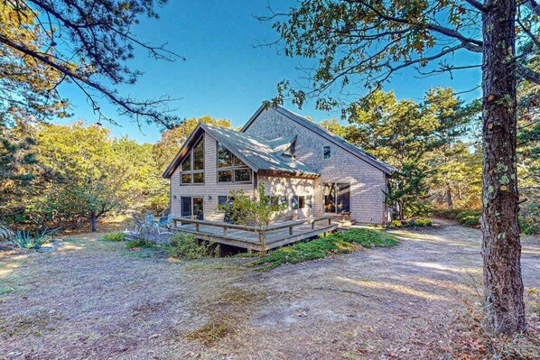 A two-story house with a deck, surrounded by trees and a clear sky.