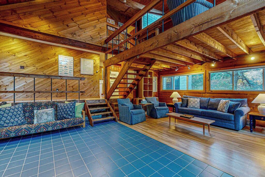 Un intérieur spacieux en bois, avec un plafond haut, un escalier et une grande fenêtre offrant une vue sur l’extérieur.