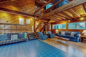 Un interior de madera espacioso con un techo alto, una escalera y un gran ventanal que ofrece vistas al exterior.