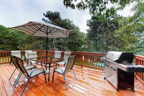 A wooden deck with a grill, a table with chairs, and an umbrella. - Split-Level, Family-Friendly Home w/ a Rear Deck, Gas Grill, Free WiFi, & W/D (Edgartown)