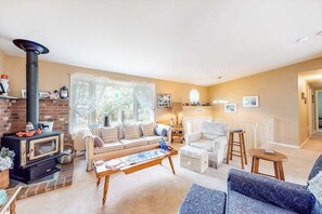 A living room with a fireplace, sofa, coffee table, and a dining area with a table and chairs. - Split-Level, Family-Friendly Home w/ a Rear Deck, Gas Grill, Free WiFi, & W/D (Edgartown)