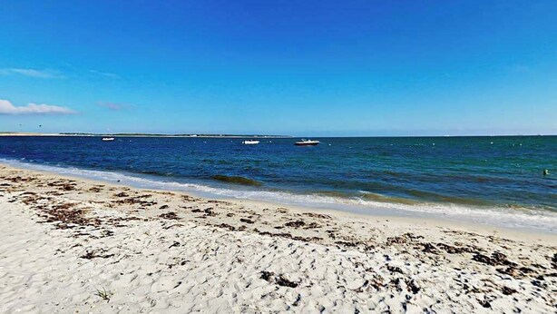 A beach with sand, water, and boats in the distance. - Expansive Getaway w/ Fenced Yard, Outdoor Shower & Private Neighborhood Beach (Hyannis)