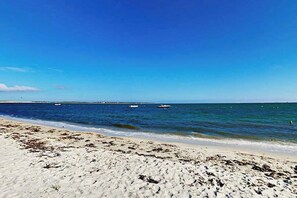 Een strand met zand, water en boten in de verte.