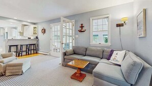 A modern living room with a gray sofa, a wooden coffee table, and a kitchen in the background. - Expansive Getaway w/ Fenced Yard, Outdoor Shower & Private Neighborhood Beach (Hyannis)