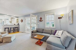A modern living room with a gray sofa, a wooden coffee table, and a kitchen in the background. - Expansive Getaway w/ Fenced Yard, Outdoor Shower & Private Neighborhood Beach (Hyannis)