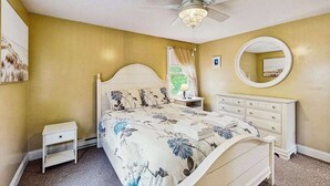 Ein Schlafzimmer mit einem Bett, einem Nachttisch, einer Kommode, einem Deckenventilator und einem runden Spiegel an der Wand.