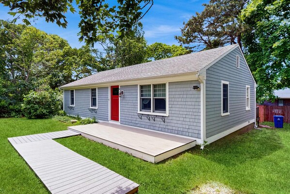 A single-story house with a red door, a small porch, and a wooden deck.