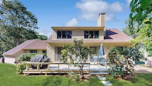 Ein zweistöckiges Haus mit überdachter Terrasse, Rasenfläche und einem kleinen Baum.