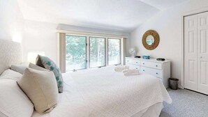 Ein Schlafzimmer mit einem großen Bett, einem Schminktisch, einem Spiegel und einem Fenster mit Blick auf Bäume.