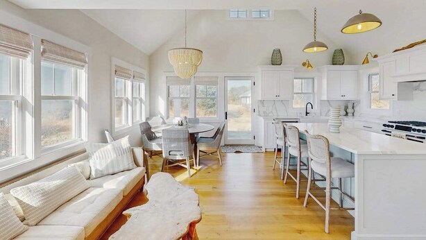 A spacious kitchen with white cabinetry, a dining area with a round table, and a seating area with a sofa and chairs. - Newly built, bayview house steps from the beach with spacious deck, W/D & grill (North Eastham)