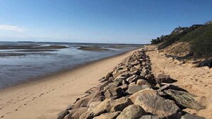 A beach with a rocky shoreline, a clear sky, and a distant view of the sea. - Newly built, bayview house steps from the beach with spacious deck, W/D & grill (North Eastham)