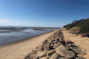 A beach with a rocky shoreline, a clear sky, and a distant view of the sea. - Newly built, bayview house steps from the beach with spacious deck, W/D & grill (North Eastham)