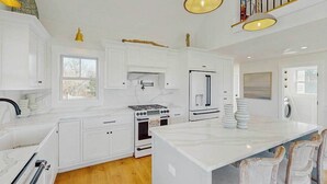 A kitchen with white cabinets, a stove, a refrigerator, and a large island. - Newly built, bayview house steps from the beach with spacious deck, W/D & grill (North Eastham)