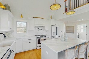 A kitchen with white cabinets, a stove, a refrigerator, and a large island. - Newly built, bayview house steps from the beach with spacious deck, W/D & grill (North Eastham)