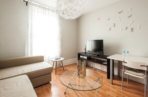 Un salon moderne avec un canapé, une table basse en verre, un téléviseur posé sur un meuble noir et un mur blanc agrémenté d’éléments décoratifs.