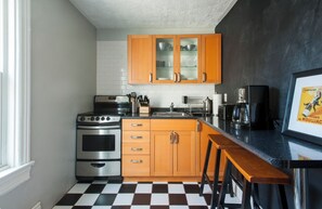 Une cuisine avec des meubles en bois, un carrelage noir et blanc, des appareils électroménagers en acier inoxydable et une affiche encadrée.