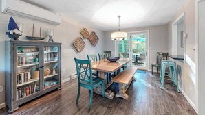Un coin repas avec une table en bois, des chaises de couleur turquoise et un meuble vitré contenant des livres.