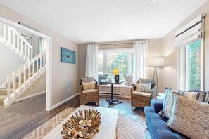 Ein Wohnzimmer mit Treppe, Korbmöbeln, einem Couchtisch mit Dekoration und Blick durch ein Fenster.