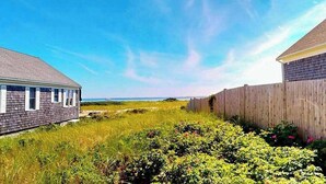 A residential area with a house, a wooden fence, and a grassy field. - Quiet cottage on the beach with deck, grill, AC, & water views (Truro)