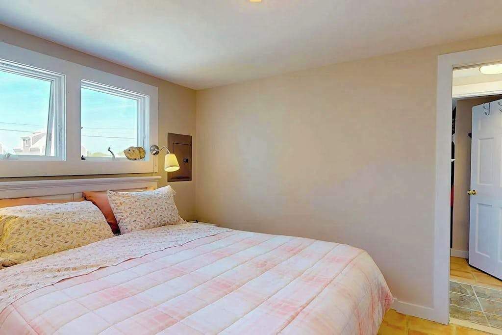 A bedroom with a bed, two windows, a door, and a nightstand.